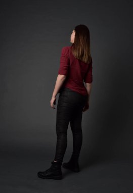 tam uzunlukta kırmızı gömlek ve deri pantolon giyen esmer kız portresi. gri studio arka plan üzerinde ayakta poz.