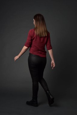 tam uzunlukta kırmızı gömlek ve deri pantolon giyen esmer kız portresi. gri studio arka plan üzerinde ayakta poz.