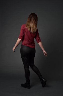 tam uzunlukta kırmızı gömlek ve deri pantolon giyen esmer kız portresi. gri studio arka plan üzerinde ayakta poz.