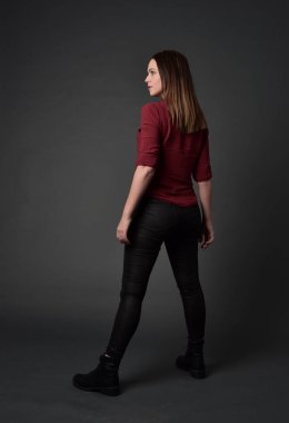 tam uzunlukta kırmızı gömlek ve deri pantolon giyen esmer kız portresi. gri studio arka plan üzerinde ayakta poz.