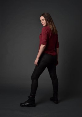 tam uzunlukta kırmızı gömlek ve deri pantolon giyen esmer kız portresi. gri studio arka plan üzerinde ayakta poz.