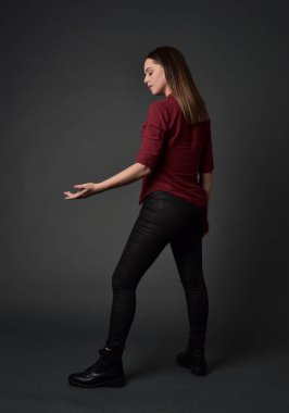 tam uzunlukta kırmızı gömlek ve deri pantolon giyen esmer kız portresi. gri studio arka plan üzerinde ayakta poz.