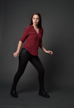 tam uzunlukta kırmızı gömlek ve deri pantolon giyen esmer kız portresi. gri studio arka plan üzerinde ayakta poz.