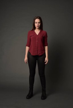 tam uzunlukta kırmızı gömlek ve deri pantolon giyen esmer kız portresi. gri studio arka plan üzerinde ayakta poz.