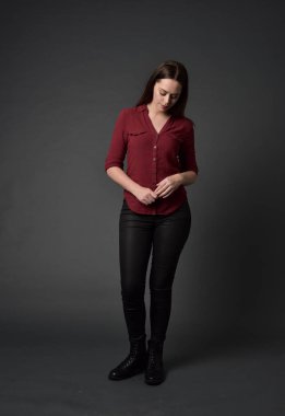 tam uzunlukta kırmızı gömlek ve deri pantolon giyen esmer kız portresi. gri studio arka plan üzerinde ayakta poz.