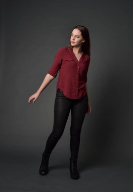 tam uzunlukta kırmızı gömlek ve deri pantolon giyen esmer kız portresi. gri studio arka plan üzerinde ayakta poz.