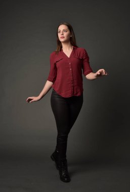 tam uzunlukta kırmızı gömlek ve deri pantolon giyen esmer kız portresi. gri studio arka plan üzerinde ayakta poz.