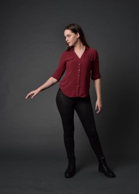 tam uzunlukta kırmızı gömlek ve deri pantolon giyen esmer kız portresi. gri studio arka plan üzerinde ayakta poz.