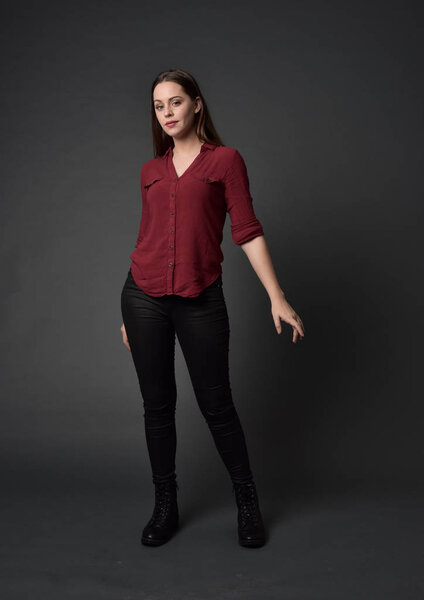 портрет брюнетки в красной рубашке и кожаных штанах. Стоя поза, на сером фоне студии
.