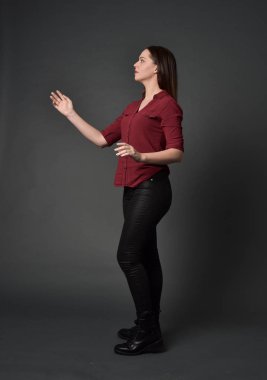 tam uzunlukta kırmızı gömlek ve deri pantolon giyen esmer kız portresi. gri studio arka plan üzerinde ayakta poz.