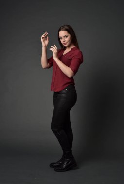 tam uzunlukta kırmızı gömlek ve deri pantolon giyen esmer kız portresi. gri studio arka plan üzerinde ayakta poz.