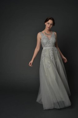 tam uzunlukta uzun gümüş topu cüppe giyen esmer kız portresi. gri studio arka plan üzerinde ayakta poz.