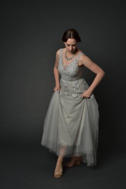 tam uzunlukta uzun gümüş topu cüppe giyen esmer kız portresi. gri studio arka plan üzerinde ayakta poz.