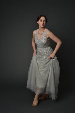 tam uzunlukta uzun gümüş topu cüppe giyen esmer kız portresi. gri studio arka plan üzerinde ayakta poz.