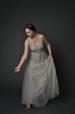 tam uzunlukta uzun gümüş topu cüppe giyen esmer kız portresi. gri studio arka plan üzerinde ayakta poz.