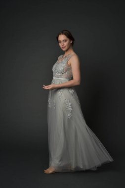 tam uzunlukta uzun gümüş topu cüppe giyen esmer kız portresi. gri studio arka plan üzerinde ayakta poz.