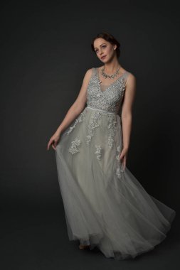 tam uzunlukta uzun gümüş topu cüppe giyen esmer kız portresi. gri studio arka plan üzerinde ayakta poz.