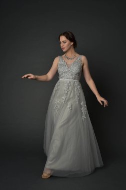 tam uzunlukta uzun gümüş topu cüppe giyen esmer kız portresi. gri studio arka plan üzerinde ayakta poz.