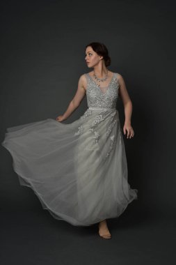 tam uzunlukta uzun gümüş topu cüppe giyen esmer kız portresi. gri studio arka plan üzerinde ayakta poz.