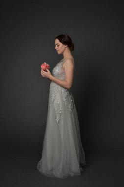 tam uzunlukta uzun gümüş topu cüppe giyen esmer kız portresi. gri studio arka plan üzerinde ayakta poz.