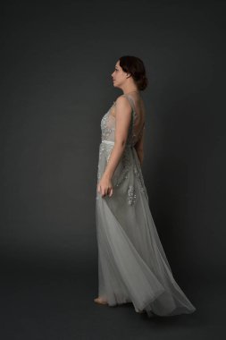 tam uzunlukta uzun gümüş topu cüppe giyen esmer kız portresi. gri studio arka plan üzerinde ayakta poz.