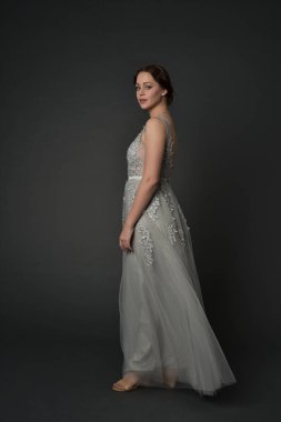 tam uzunlukta uzun gümüş topu cüppe giyen esmer kız portresi. gri studio arka plan üzerinde ayakta poz.