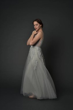 tam uzunlukta uzun gümüş topu cüppe giyen esmer kız portresi. gri studio arka plan üzerinde ayakta poz.