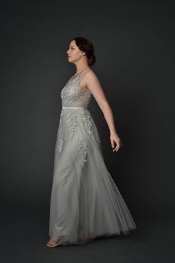 tam uzunlukta uzun gümüş topu cüppe giyen esmer kız portresi. gri studio arka plan üzerinde ayakta poz.