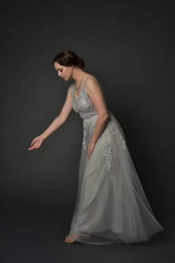 tam uzunlukta uzun gümüş topu cüppe giyen esmer kız portresi. gri studio arka plan üzerinde ayakta poz.