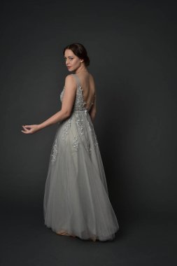 tam uzunlukta uzun gümüş topu cüppe giyen esmer kız portresi. gri studio arka plan üzerinde ayakta poz.