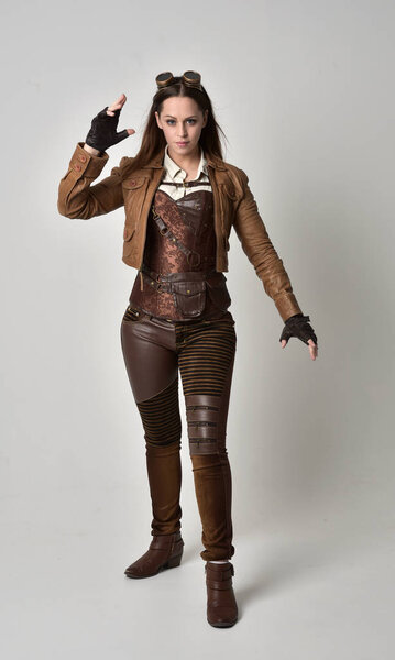 full length portrait of brunette  girl wearing brown leather steampunk outfit. standing pose on grey studio background.