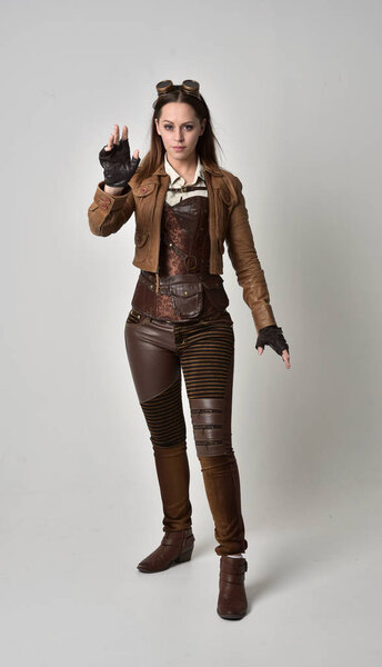 full length portrait of brunette  girl wearing brown leather steampunk outfit. standing pose on grey studio background.