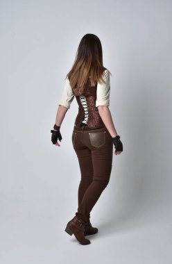 tam uzunlukta kahverengi deri steampunk kıyafeti giymiş esmer kız portresi. ayakta poz ile kameranın arkasında gri studio arka plan.