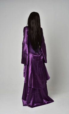 tam uzunlukta portresi uzun siyah saçlı güzel kız mor fantezi Ortaçağ elbisesi giyiyor. gri studio arka plan üzerinde ayakta poz.