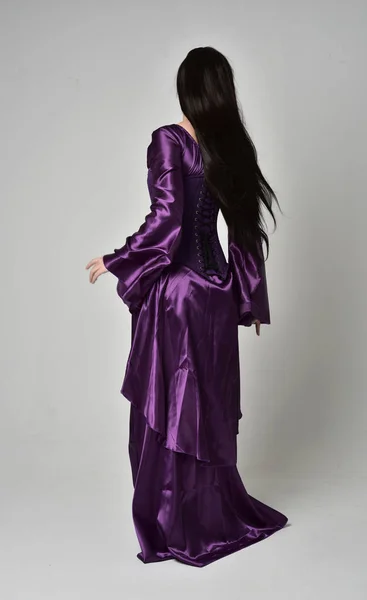 紫ファンタジー中世ガウンを身に着けている長い黒髪の美しい少女の完全な長さの肖像画 灰色のスタジオの背景に立ちポーズ — ストック写真