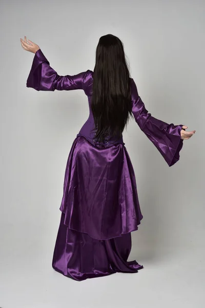 长黑色头发的美丽女孩的全长肖像 穿着紫色幻想中世纪的礼服 站在灰色工作室背景的姿势 — 图库照片