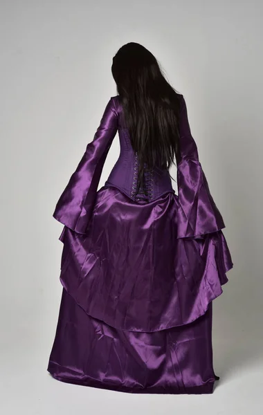 紫ファンタジー中世ガウンを身に着けている長い黒髪の美しい少女の完全な長さの肖像画 灰色のスタジオの背景に立ちポーズ — ストック写真