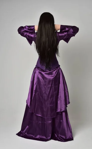长黑色头发的美丽女孩的全长肖像 穿着紫色幻想中世纪的礼服 站在灰色工作室背景的姿势 — 图库照片