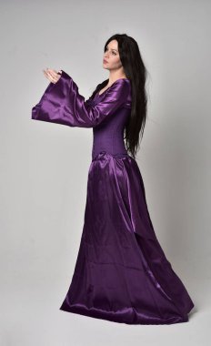 tam uzunlukta portresi uzun siyah saçlı güzel kız mor fantezi Ortaçağ elbisesi giyiyor. gri studio arka plan üzerinde ayakta poz.