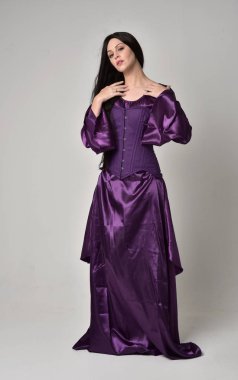 tam uzunlukta portresi uzun siyah saçlı güzel kız mor fantezi Ortaçağ elbisesi giyiyor. gri studio arka plan üzerinde ayakta poz.