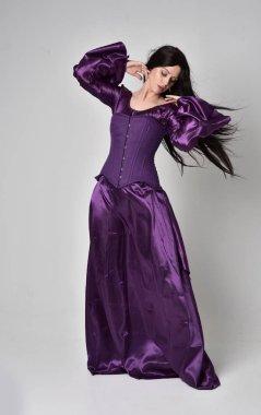 tam uzunlukta portresi uzun siyah saçlı güzel kız mor fantezi Ortaçağ elbisesi giyiyor. gri studio arka plan üzerinde ayakta poz.