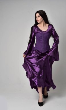 tam uzunlukta portresi uzun siyah saçlı güzel kız mor fantezi Ortaçağ elbisesi giyiyor. gri studio arka plan üzerinde ayakta poz.