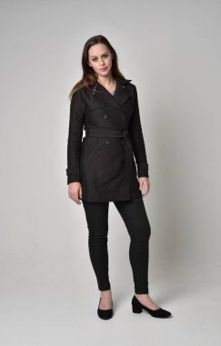 uzun, siyah ceket, gri studio arka plan üzerinde ayakta poz giyen bir esmer kız portresi tam uzunlukta.