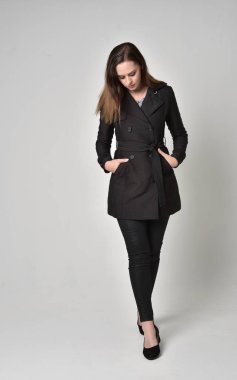 uzun, siyah ceket, gri studio arka plan üzerinde ayakta poz giyen bir esmer kız portresi tam uzunlukta.