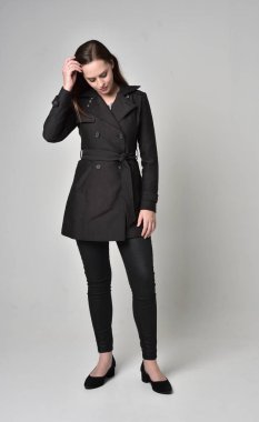 uzun, siyah ceket, gri studio arka plan üzerinde ayakta poz giyen bir esmer kız portresi tam uzunlukta.