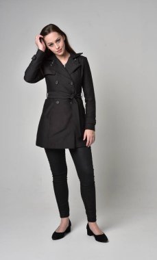 uzun, siyah ceket, gri studio arka plan üzerinde ayakta poz giyen bir esmer kız portresi tam uzunlukta.