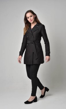 uzun, siyah ceket, gri studio arka plan üzerinde ayakta poz giyen bir esmer kız portresi tam uzunlukta.