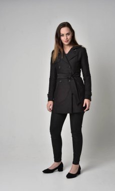 uzun, siyah ceket, gri studio arka plan üzerinde ayakta poz giyen bir esmer kız portresi tam uzunlukta.