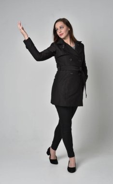 uzun, siyah ceket, gri studio arka plan üzerinde ayakta poz giyen bir esmer kız portresi tam uzunlukta.