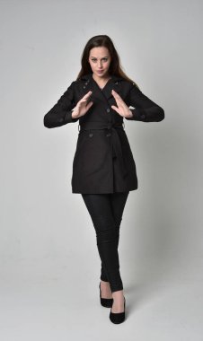 uzun, siyah ceket, gri studio arka plan üzerinde ayakta poz giyen bir esmer kız portresi tam uzunlukta.